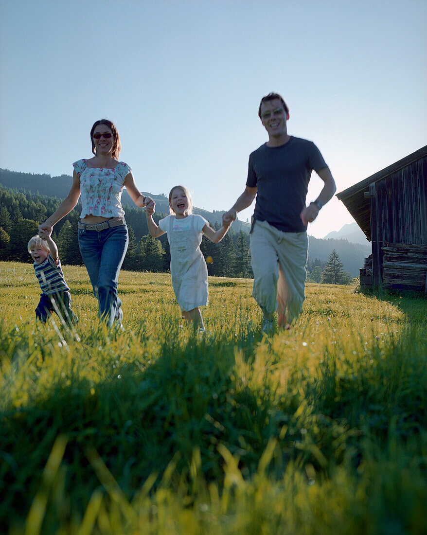 Familie mit zwei Kindern läuft über eine Bergwiese, Leogang, Salzburg, Österreich
