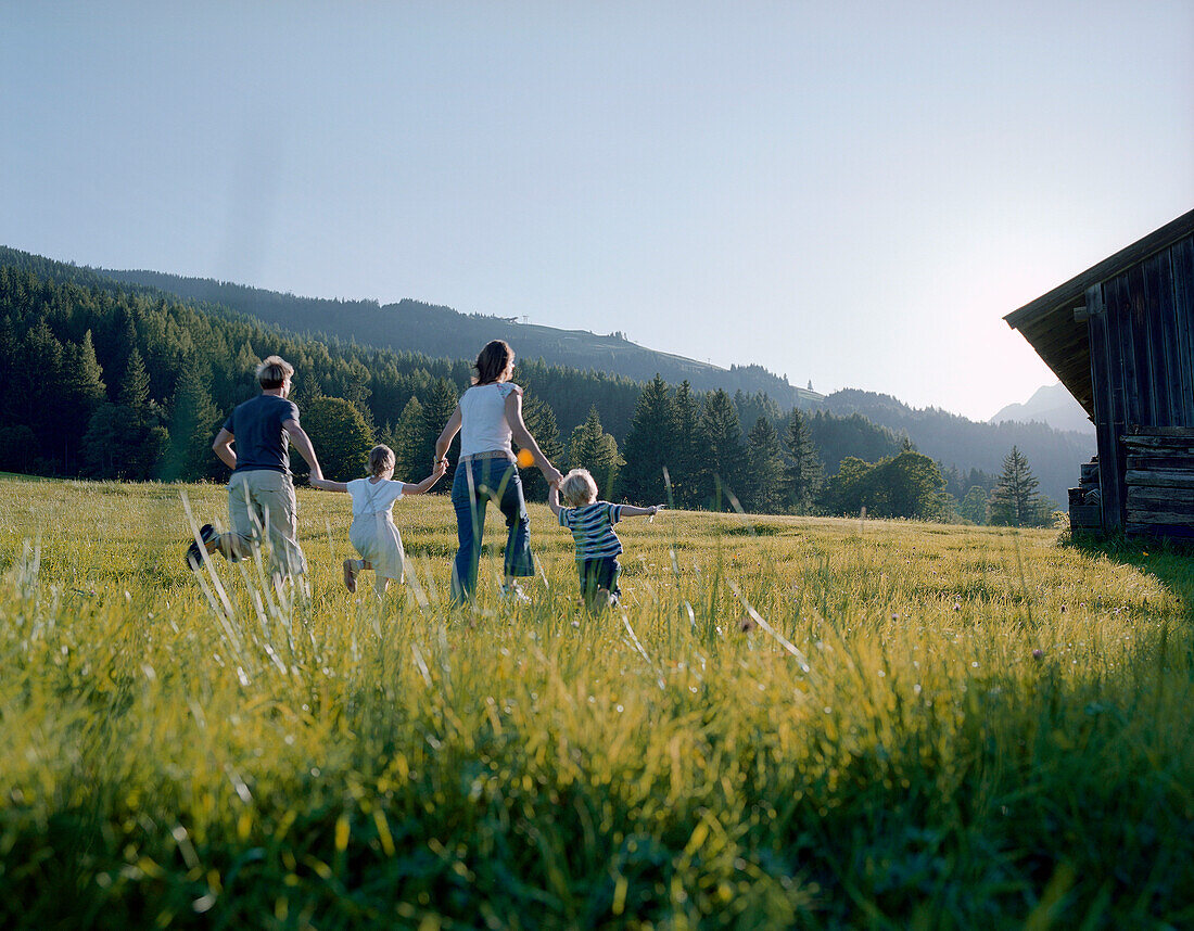 Familie mit zwei Kindern rennt über eine Bergwiese, Leogang, Salzburg, Österreich