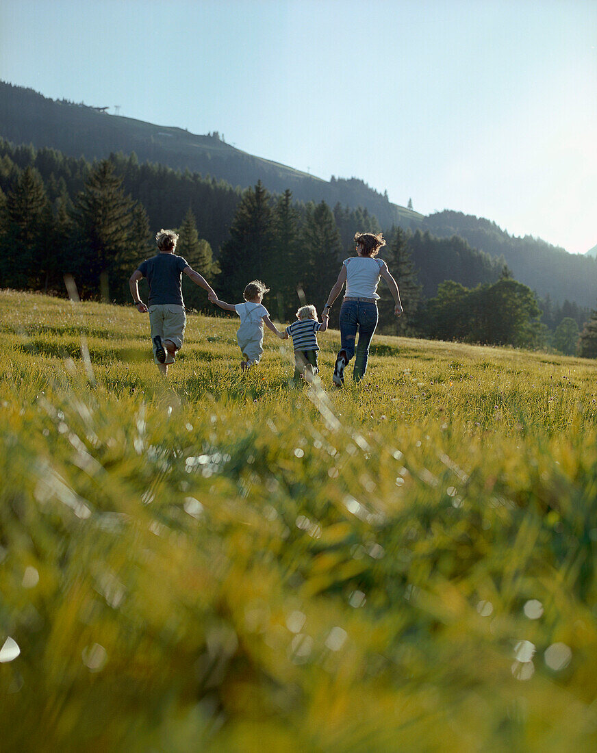 Familie mit zwei Kindern läuft über Bergwiese, Leogang, Salzburg, Österreich