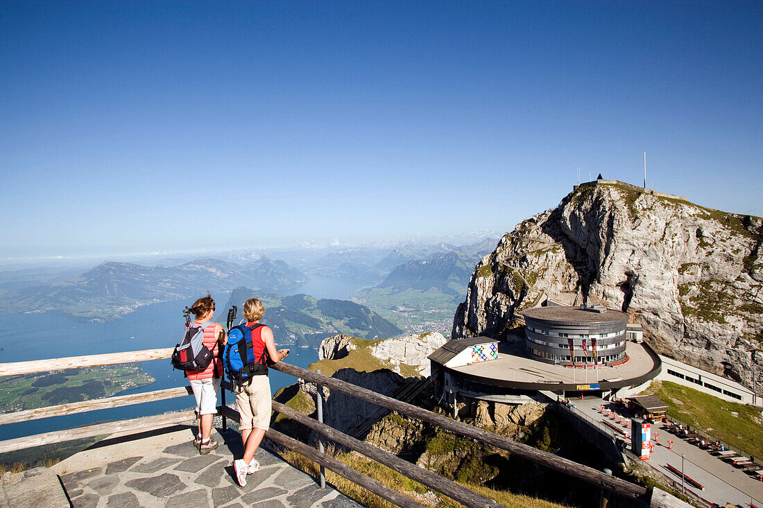 Two female hikers standing on vantage point looking to Hotel Bellevue in front of mount Esel (2118 m), panoramic view over Lake Lucerne, Pilatus (2132 m), Pilatus Kulm, Canton of Obwalden, Switzerland