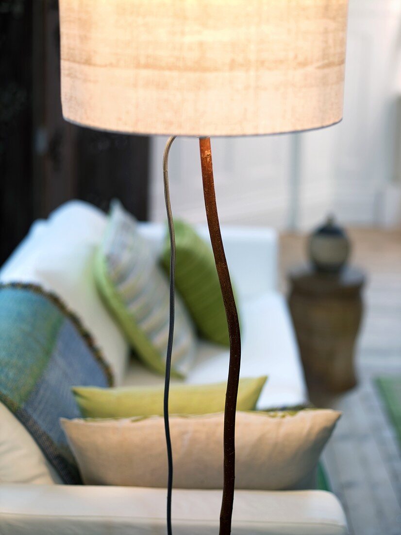 Floor lamp wit light colored shade in front of a sofa