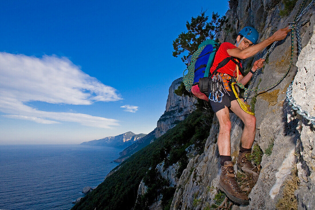 Ein junger Mann klettert mit Hilfe einer Kette, Il Sentiereo Selvaggio Blu, Golfo di Orosei, Sardinien, Italien