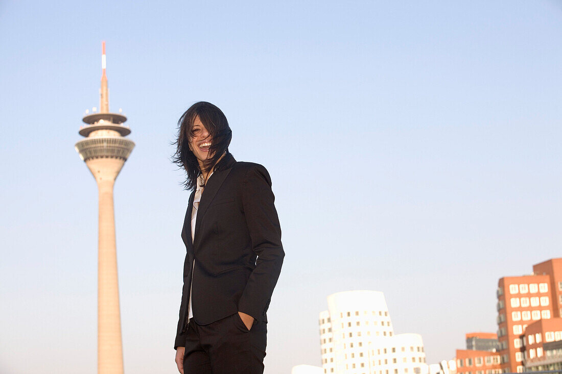 Young business woman in front of the city skyline with television tower, Zollhof, at the Media Harbour, architecture of Frank O.Gehry, Düsseldorf, state capital of NRW, North-Rhine-Westphalia, Germany