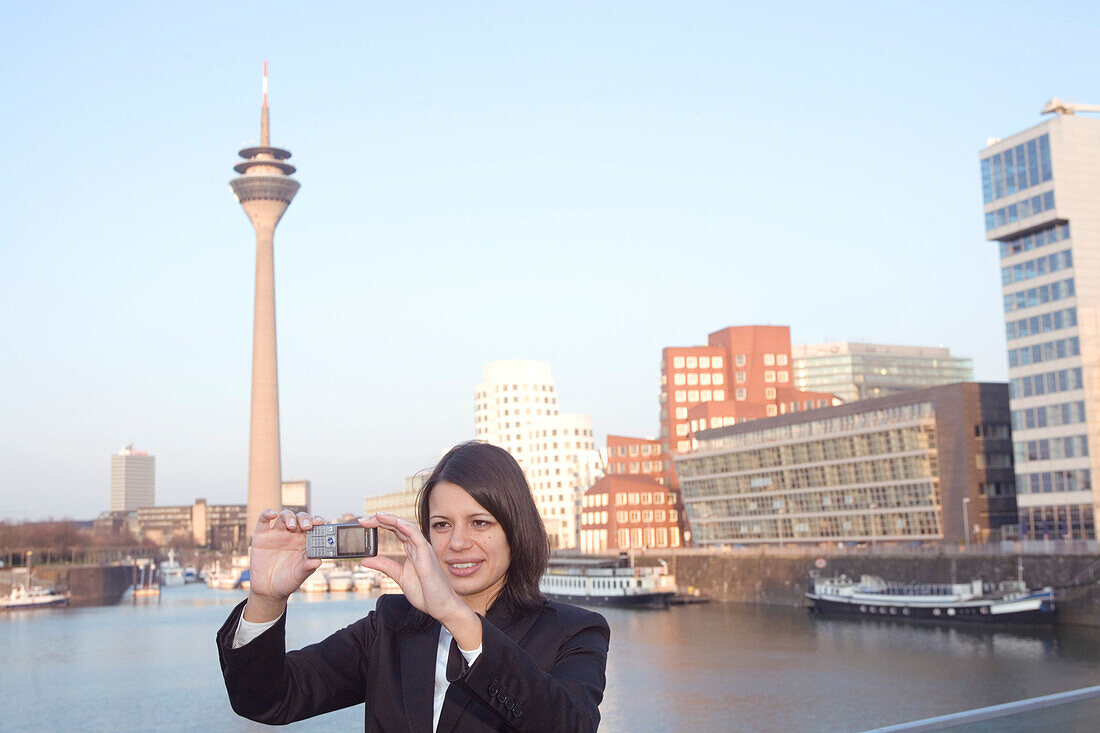 Junge Geschäftsfrau fotografiert sich selbst mit Handy, Fernsehturm, Rheinturm, Neuer Zollhof, Medienhafen von Düsseldorf, Landeshauptstadt von NRW, Deutschland