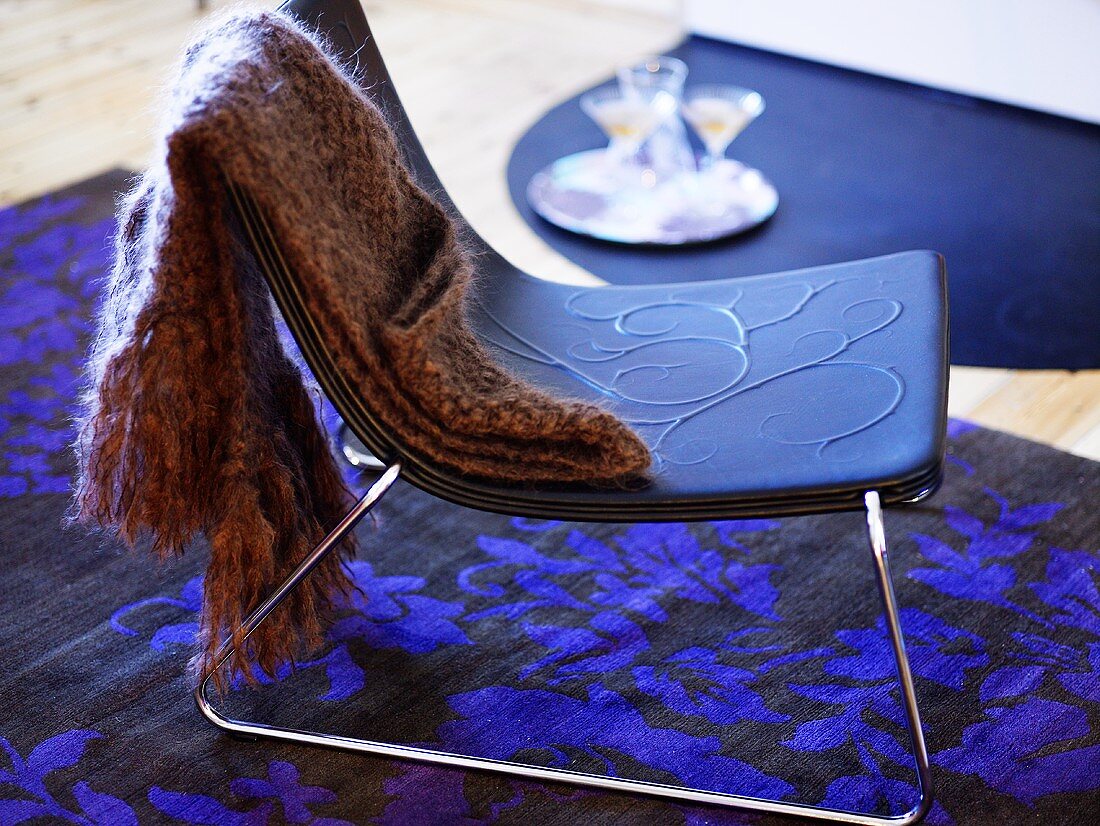 Wool shawl on a stool with blue seat and stainless steel frame on a black and blue carpet with floral pattern