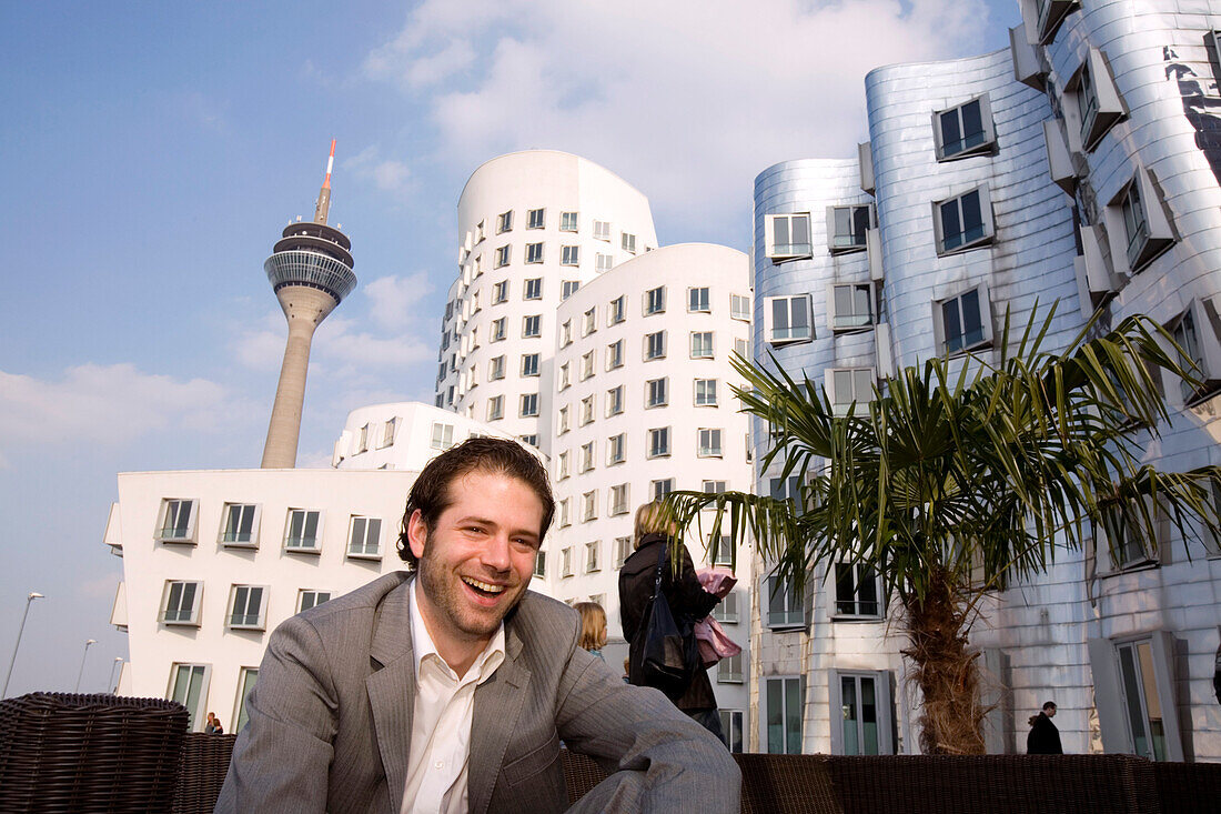 Junger Mann vor Neuem Zollhof, Architektur von Frank O.Gehry, mit Fernsehturm, Rheinturm im Hintergrund, Medienhafen in Düsseldorf, Nordrhein-Westfalen, Landeshauptstadt in NRW, Deutschland
