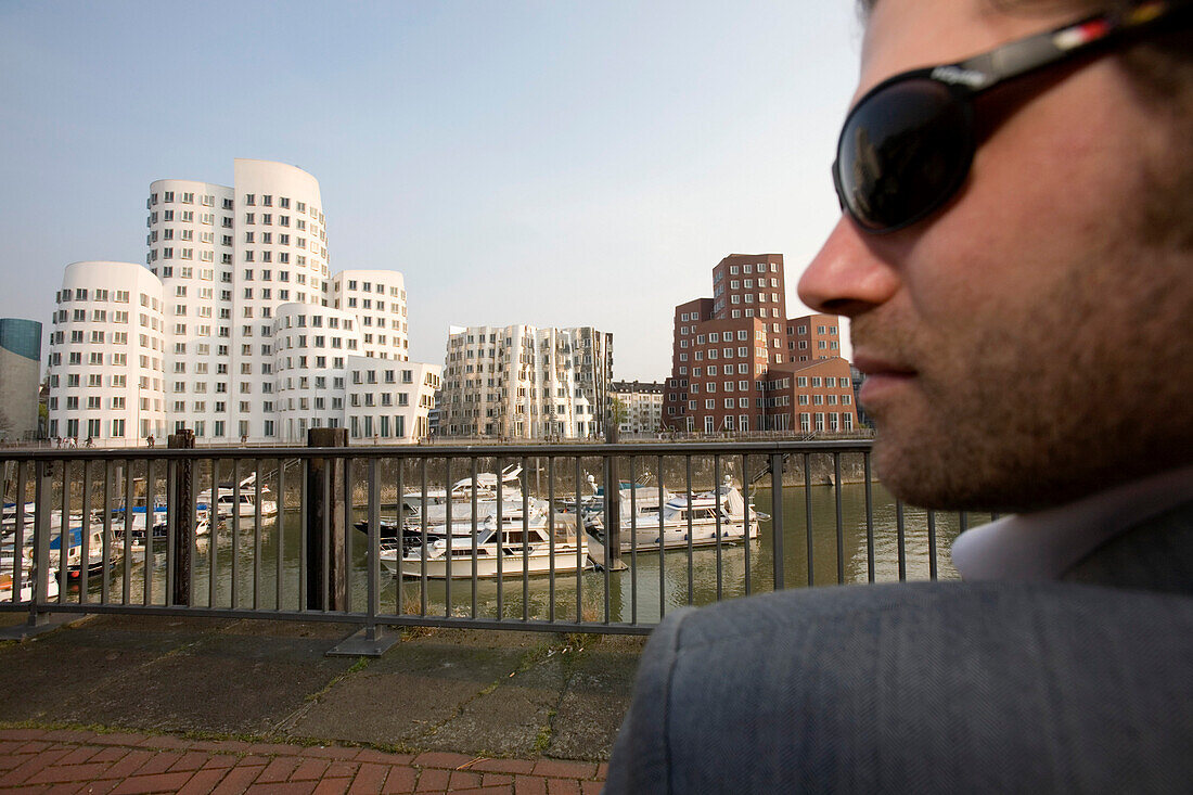 Junger Mann mit Sonnenbrille, Neuer Zollhof, Architektur von Frank O.Gehry, Medienhafen in Düsseldorf, Nordrhein-Westfalen, Landeshauptstadt in NRW, Deutschland