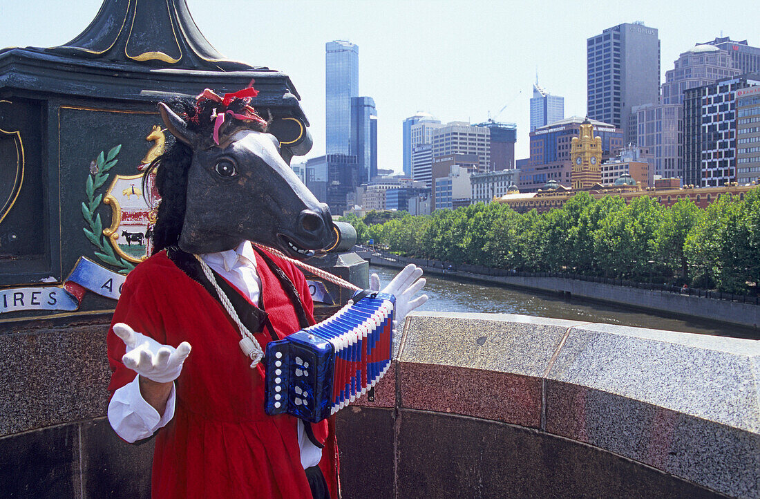 Kostümierter Musikant in der Swanston Road mit dem Yarra River und der Skyline von Melbourne im Hintergrund