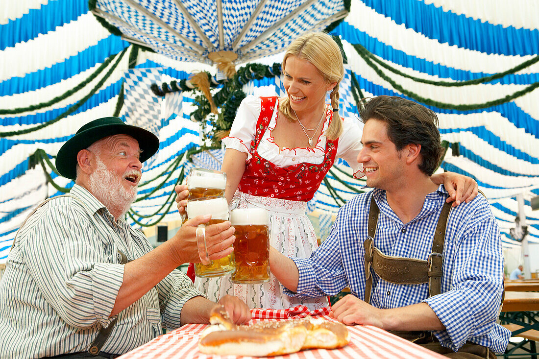 Paar und ein älterer Mann stoßen mit Bier im Bierzelt an