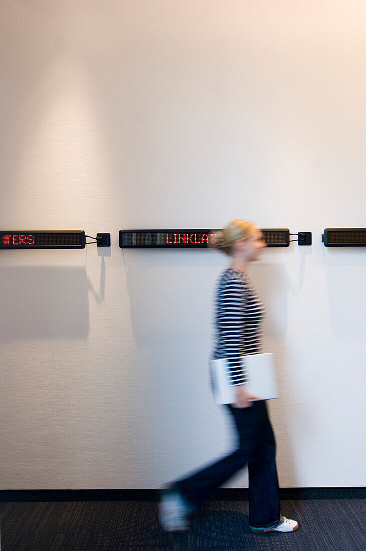 Young woman walks down hallway with laptop, Luxembourg