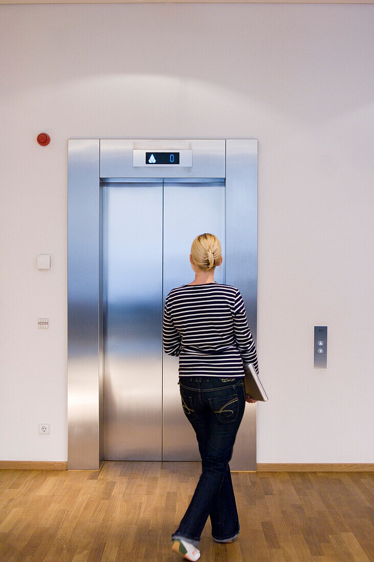 Young woman carrying a laptop standing in front of an elevator, Luxembourg