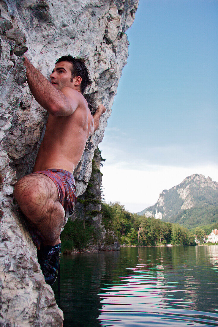 Young man climbing, Lake Alpsee, Schwangau, Bavaria, Germany