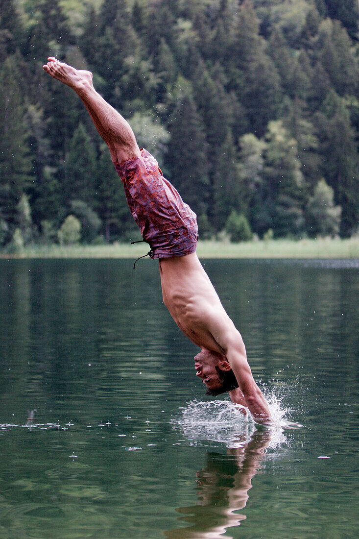Young man jumping into a lake, Fuessen, Bavaria, Germany