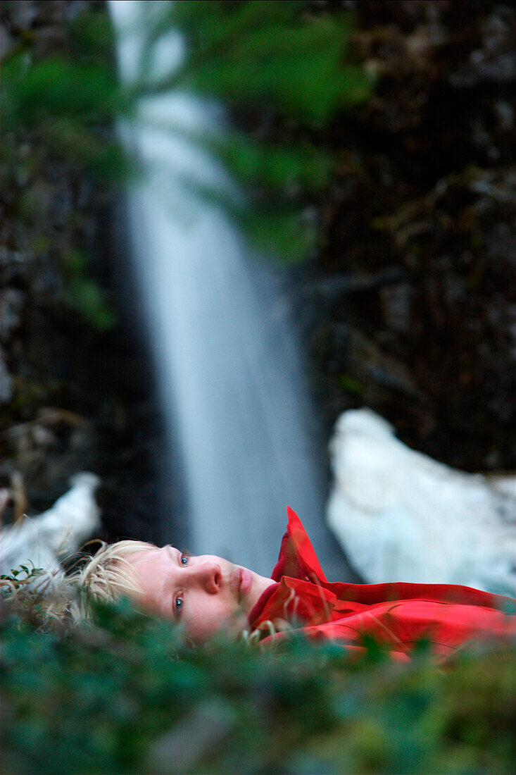Junge Frau liegt im Gras vor einem Wasserfall, See, Tirol, Österreich