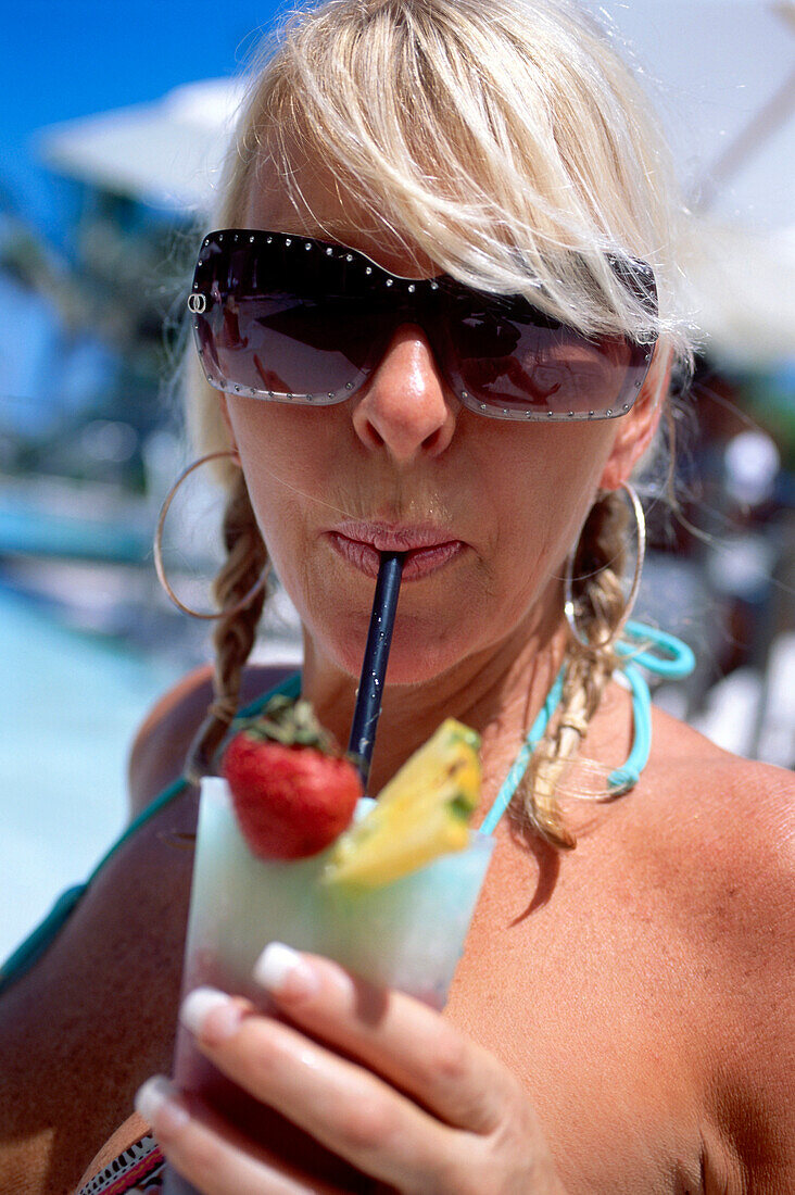 Blond woman with sunglasses having a cocktail on the beach, South Beach, Miami, Florida, USA