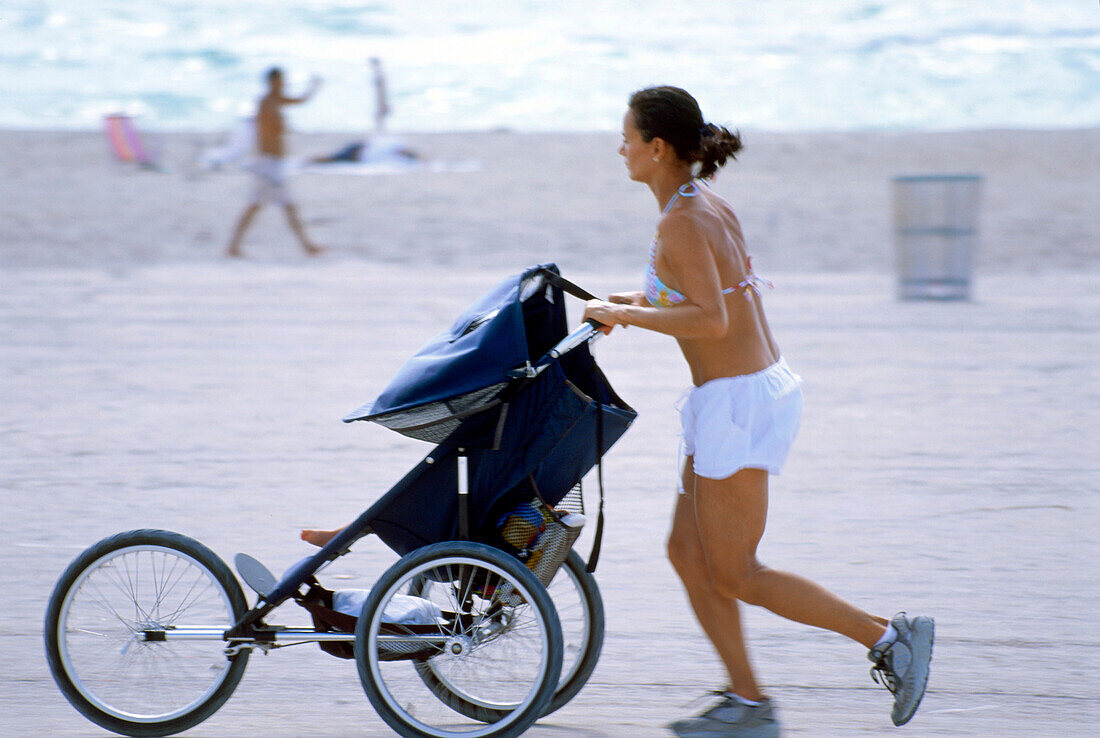 Frau mit Kinderwagen beim Joggen am Strand, South Beach, Miami, Florida, USA