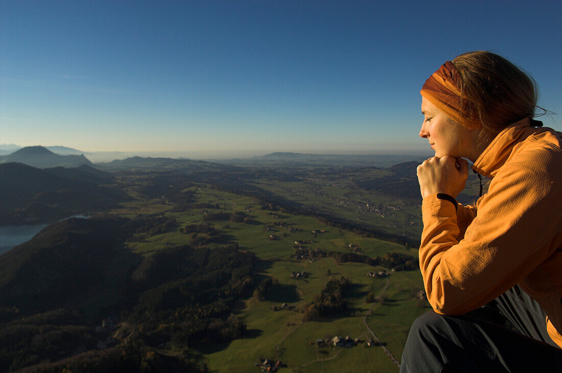 Woman with closed eyes sitting on top of mount Schoberstein, Lake Fuschl in background, Salzkammergut, Upper Austria, Austria