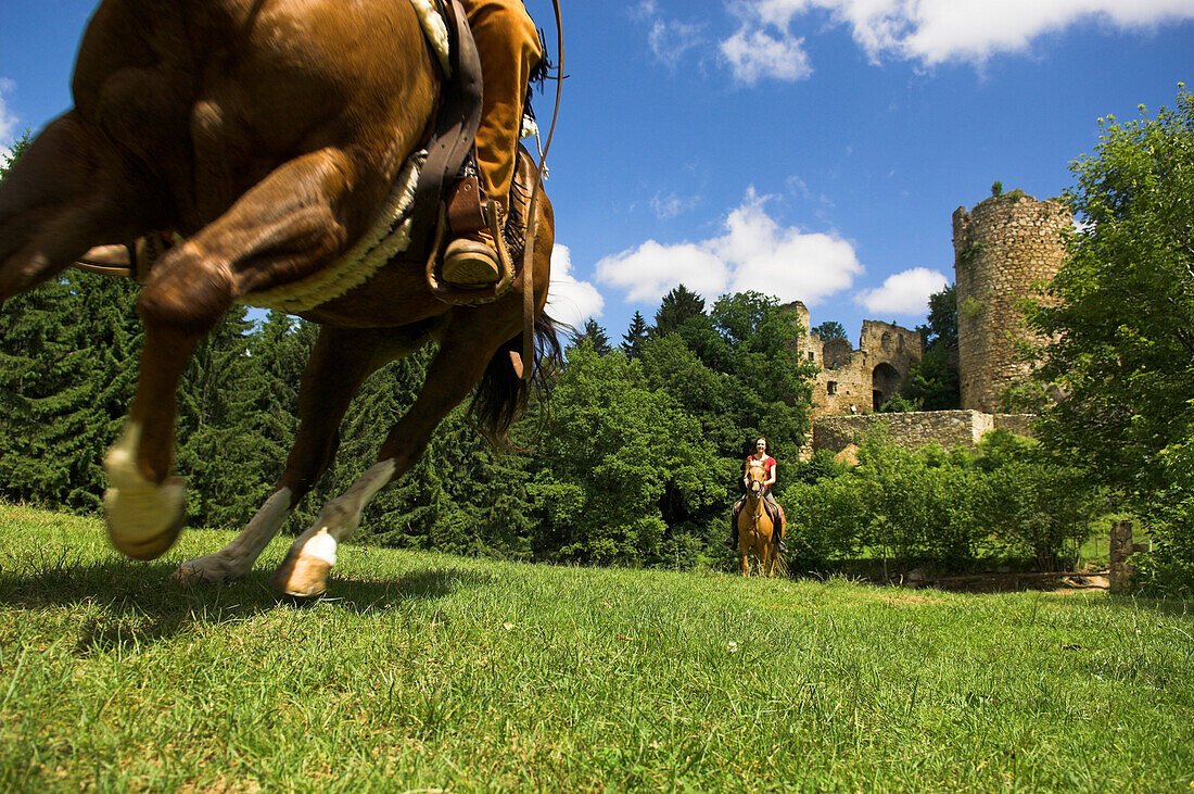 Two horseriders galloping over a field, Castle Brandegg ruins in the background, Muehlviertel, Upper Austria, Austria