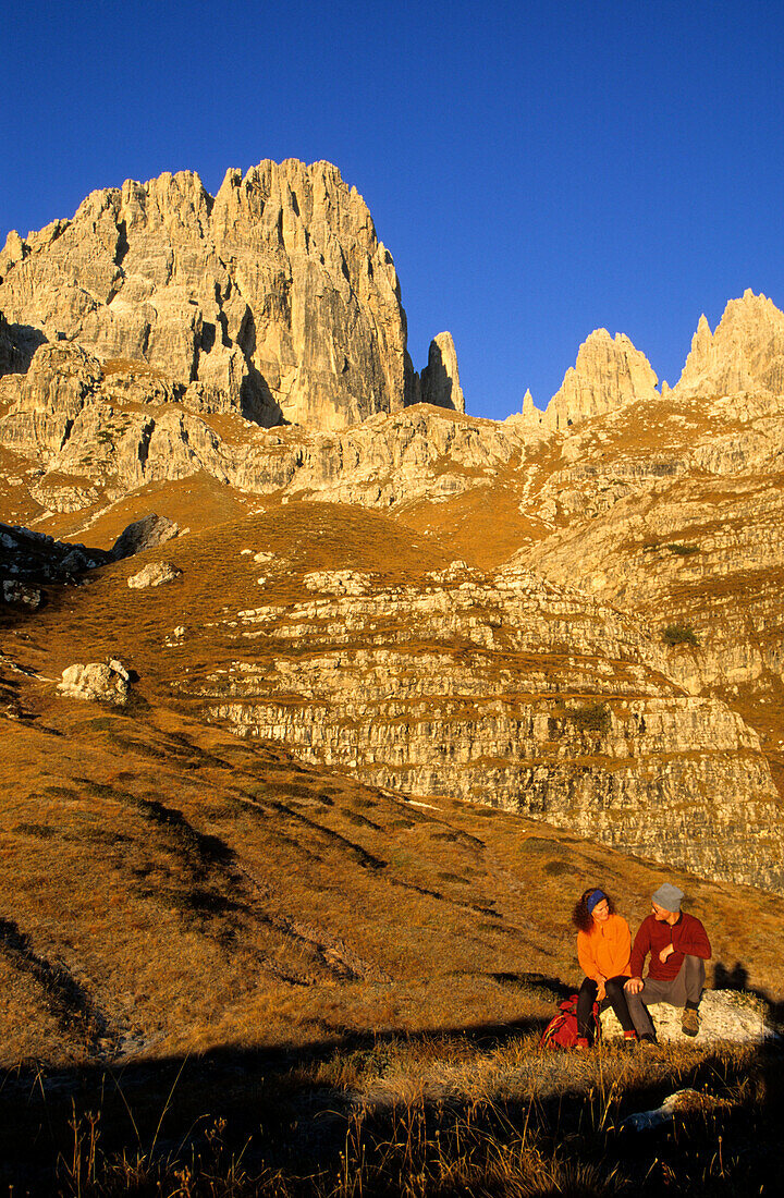 Couple in front of the rock faces of Cima Brenta alta and Guglia di Brenta, Brenta Range, Italy