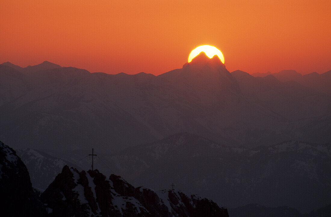 sun behind summit of Guffert with pinnacles with crosses on summit in foreground, Kaiser range, Tyrol, Austria