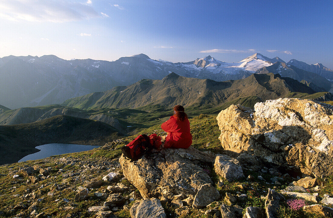 Hiker resting at Pluderlingsattel with view to lake Junsee, Gefrorene Wandspitzen and Olperer, Tuxer range, Tyrol, Austria