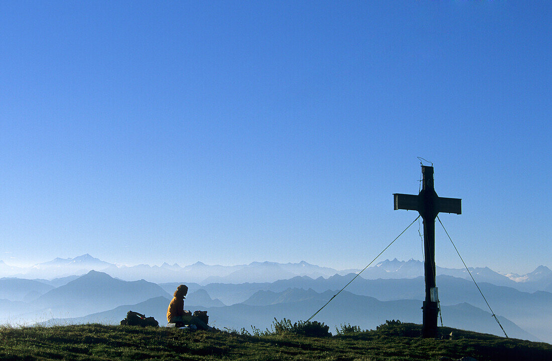 Hiker at cross on summit of Sonnwendjoch, Rofan range, Tyrol, Austria