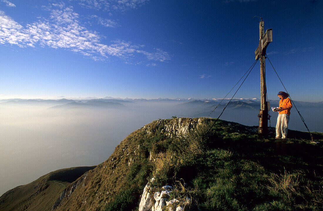 Hiker at cross on summit of Sonnwendjoch, fogbank in the valley of Inn, Rofan range, Tyrol, Austria