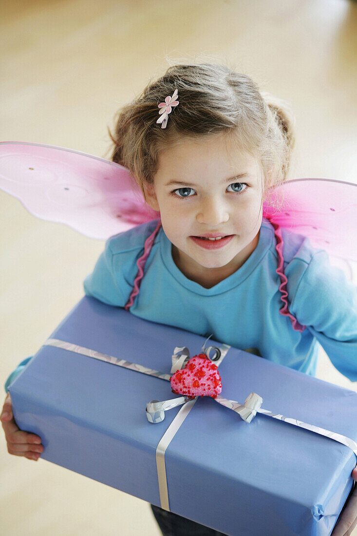 Mädchen (3-4 Jahre) mit Schmetterlingsflügeln und Geschenk