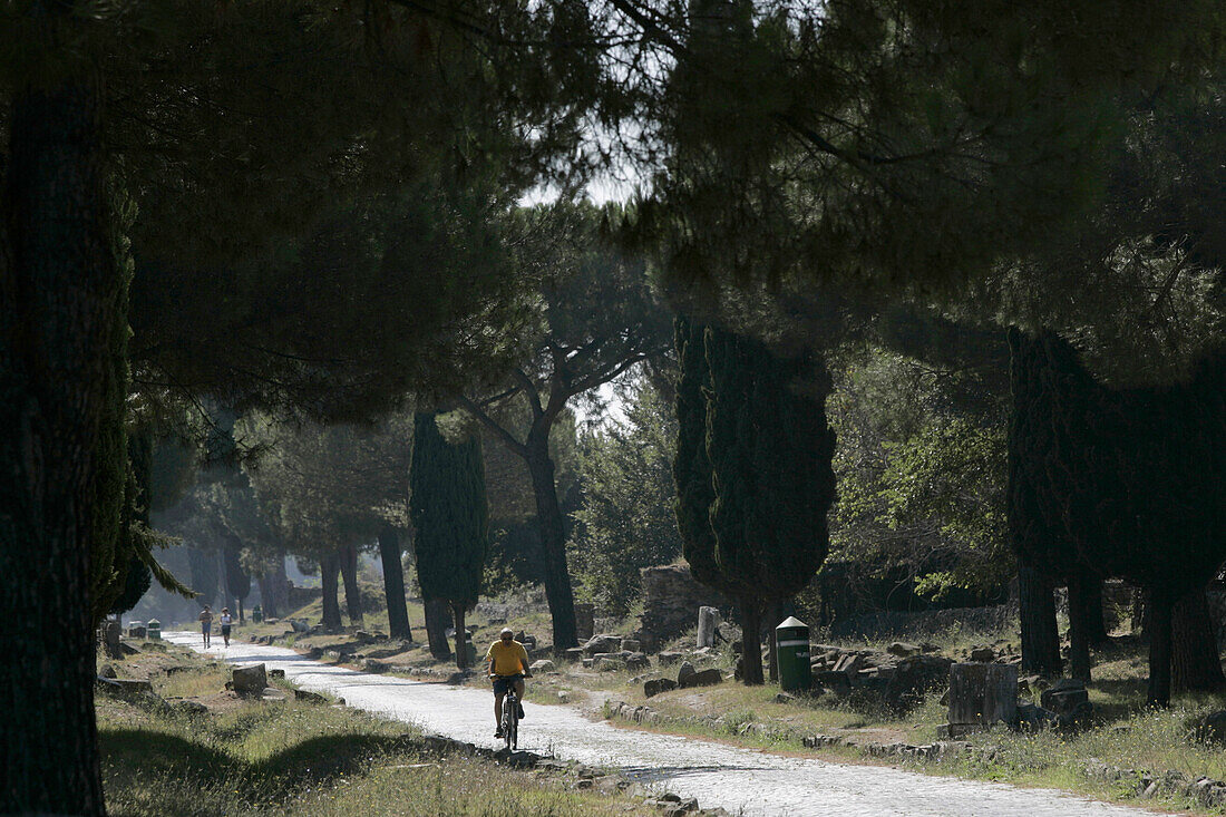 Man fährt mit seinem Fahrrad auf der kaputten römischen Via Appia Antica Strasse, Rom, Italien