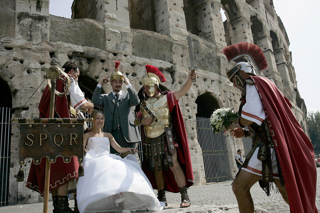 Hochzeitspaar posiert für den Hochzeitsfotografen vor dem Kolosseum mit Männern die als römische Soldaten verkleidet sind, Rom, Itallien