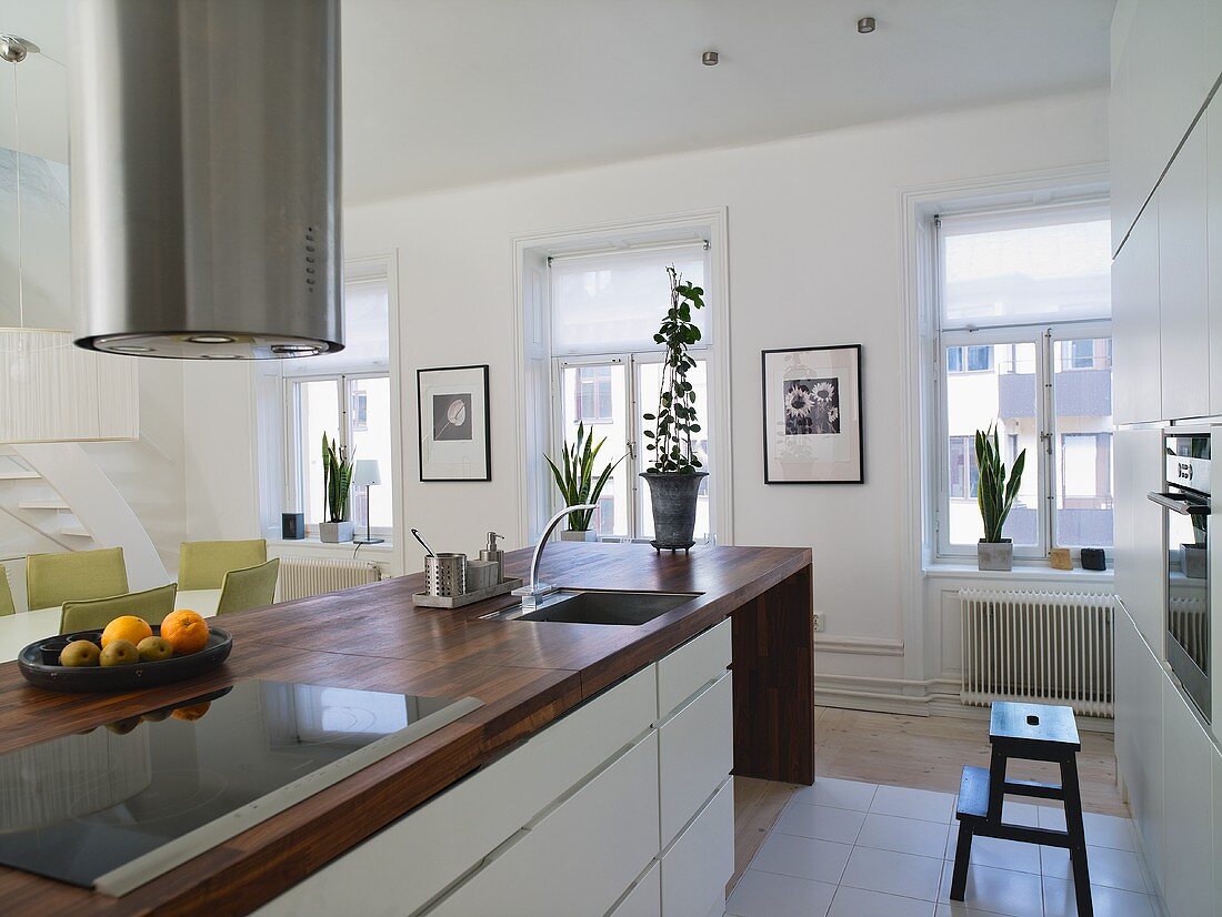 weiße Designerküche - Edelstahlabzug über Küchenblock mit Holzarbeitsplatte und Fensterfront