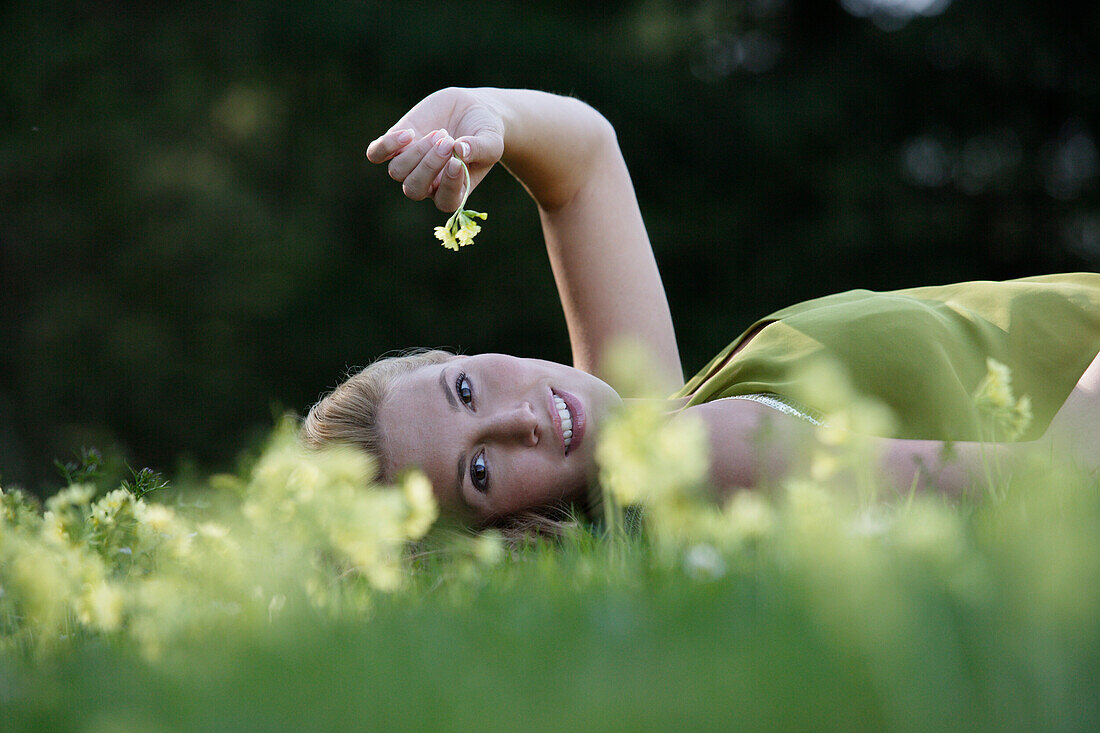 Junge Frau liegt auf einer Blumenwiese und lächelt in die Kamera, Icking, Bayern, Deutschland