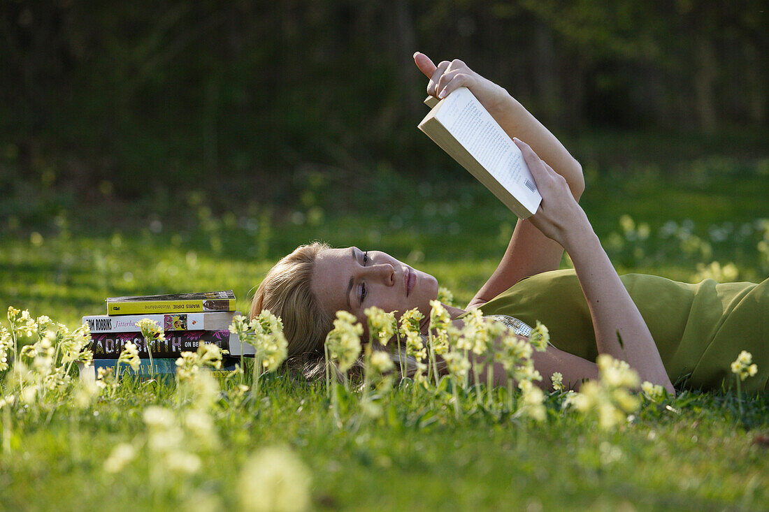 Junge Frau liegt auf einer Wiese und liest ein Bauch, Icking, Bayern, Deutschland