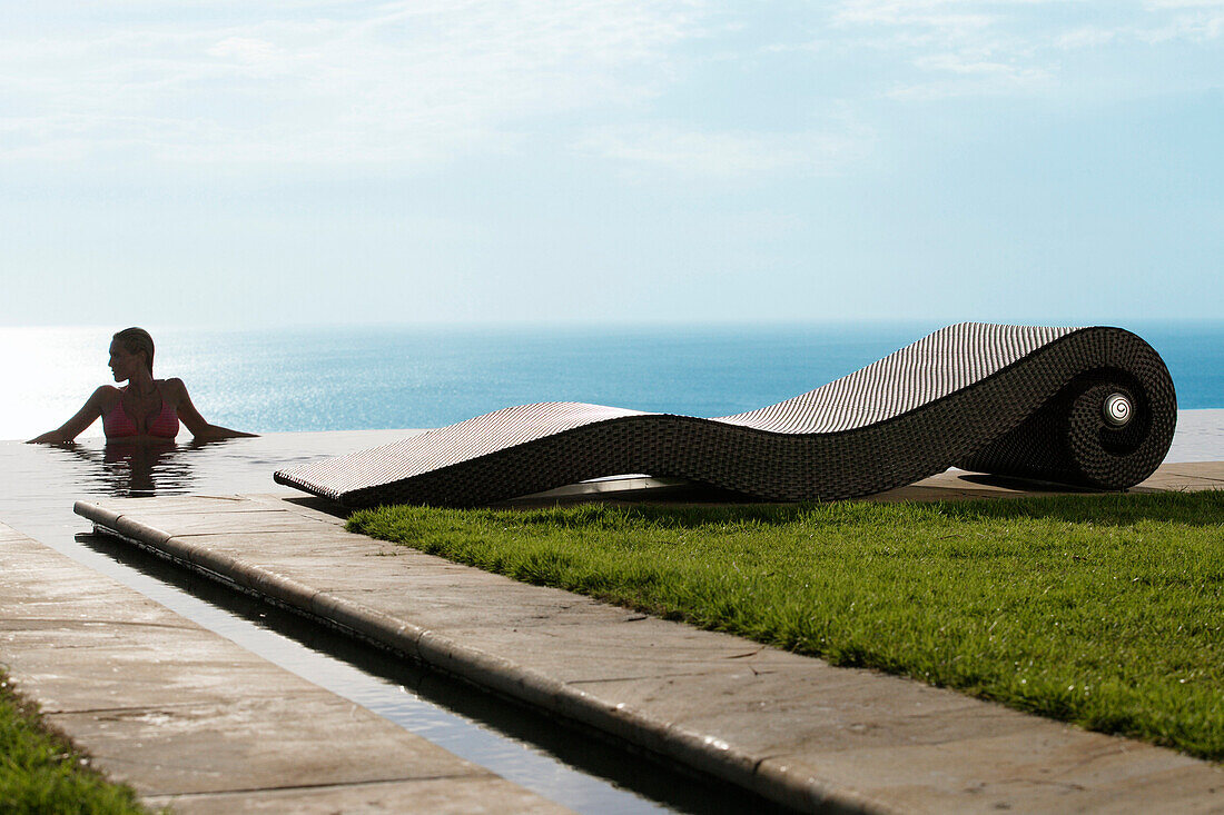 Eine Frau im Pool mit Blick auf das Meer, nahe Uluwatu, Bali, Indonesien