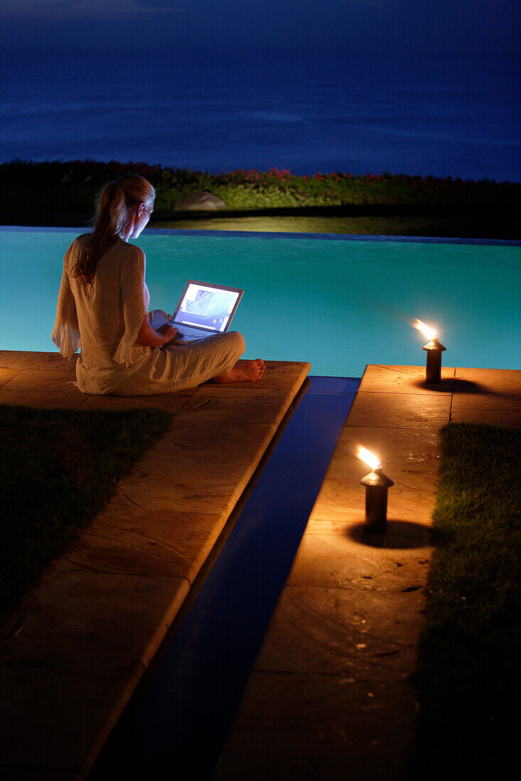 Junge Frau sitzt mit Laptop am Pool, nahe Uluwatu, Bali, Indonesien