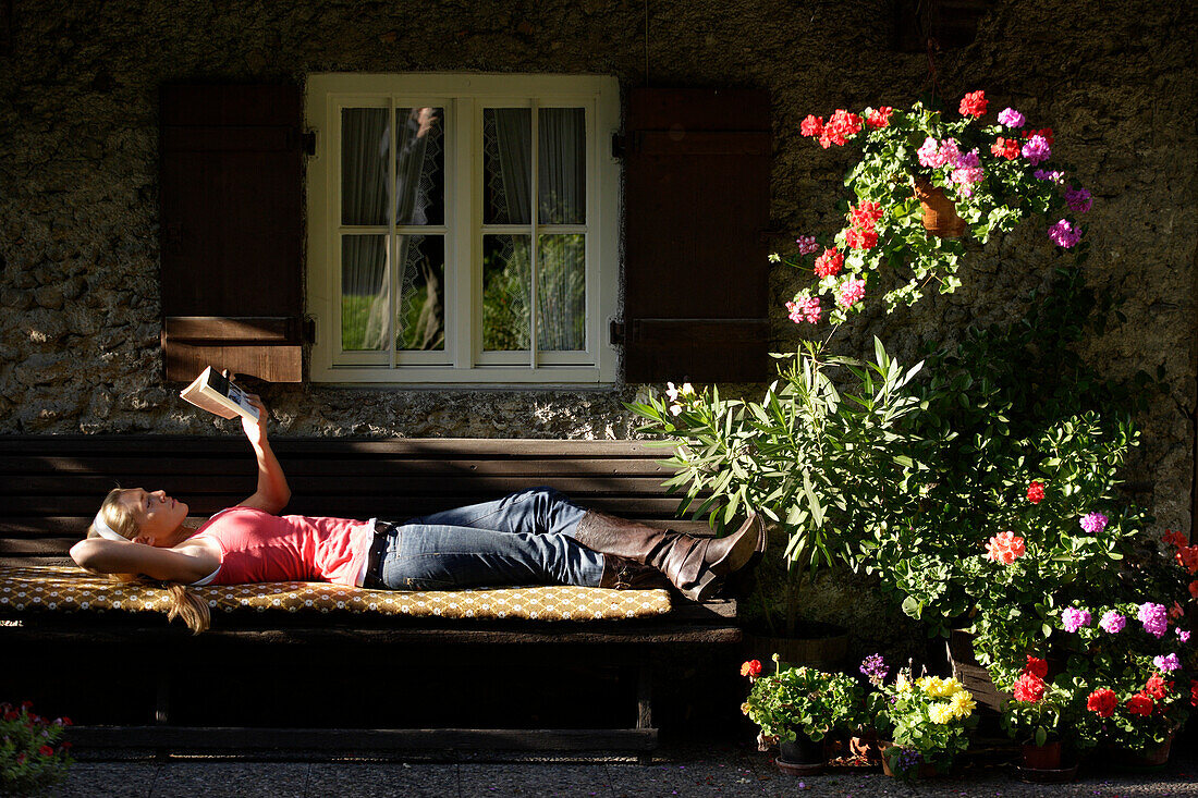 Youg woman lying on a bench while reading a book, Brannenburg, Upper Bavaria, Bavaria, Germany