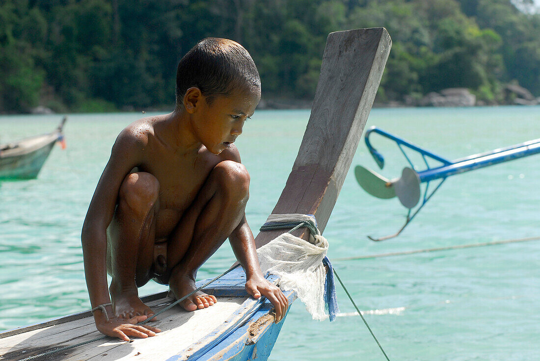 Child, boy, crouching on a boat, Chao Naam, Moken, Surin Islands Marine National Park, Ko Surin Noi, Phang Nga, Thailand