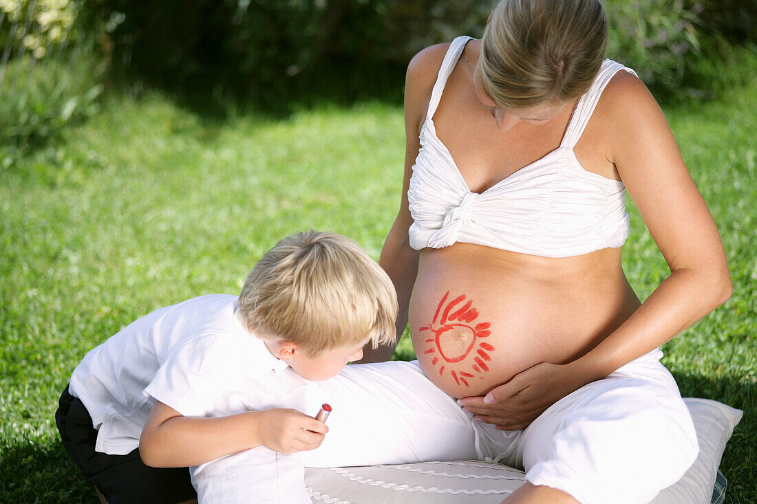 Junge (4-5 Jahre) malt Sonne auf Bauch einer schwangeren Frau, Steiermark, Österreich