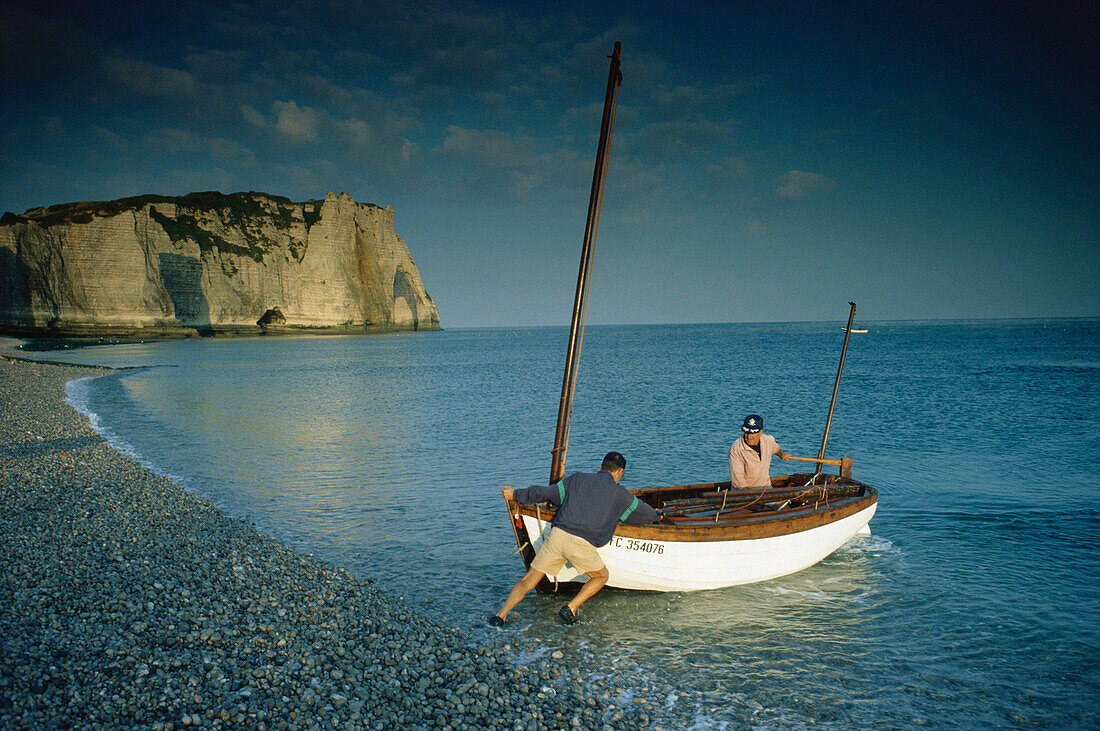 Two men pushing fishing boat into the water, Falaise, d´Aval, Etretat, Normandy, France