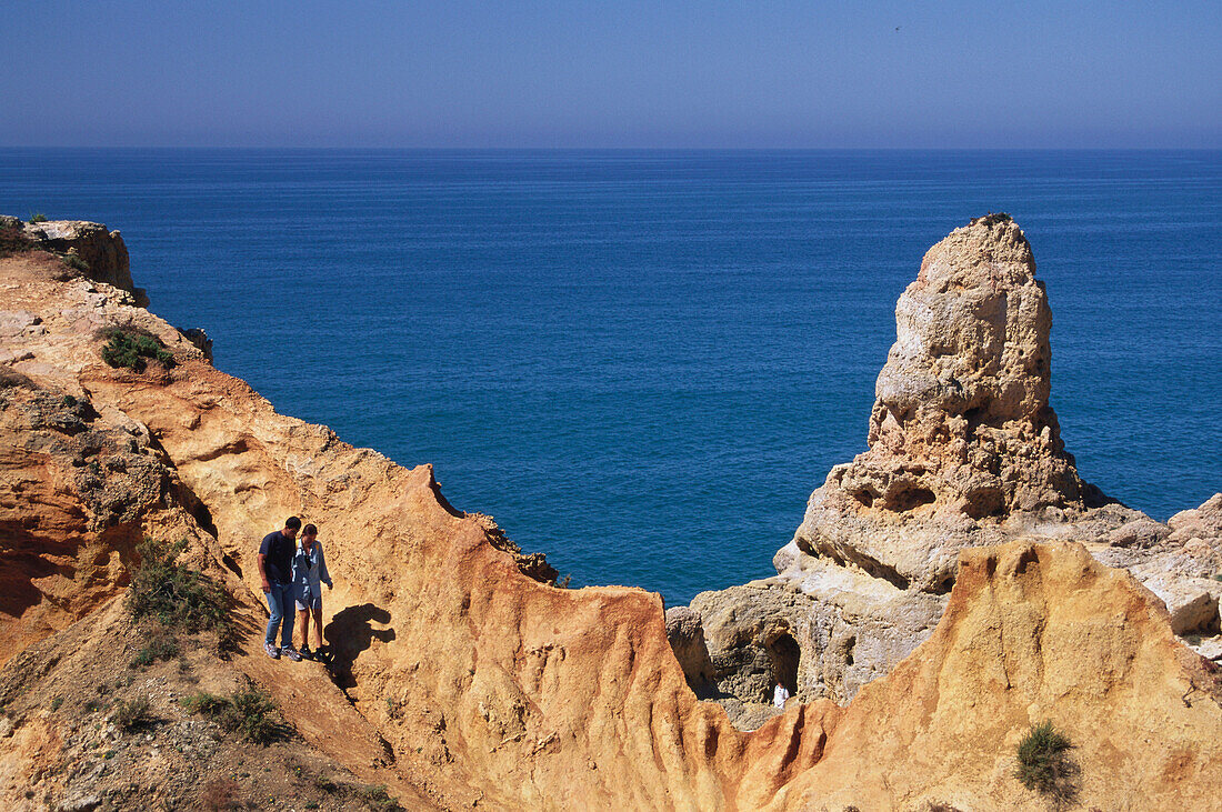 A couple walking along limestone rock, Algar Seco, Carvoeiro, Algarve, Portugal
