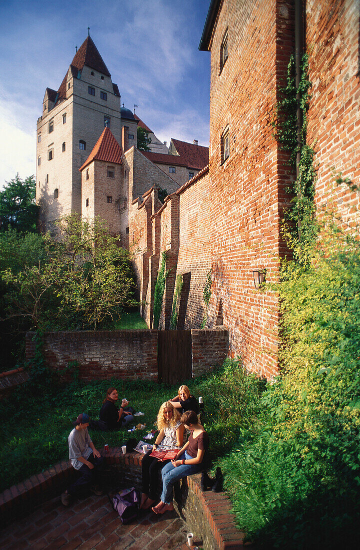 Young people having a picnic beneath the tall walls and towers of Trausnitz castle, Landshut, Lower Bavaria, Germany