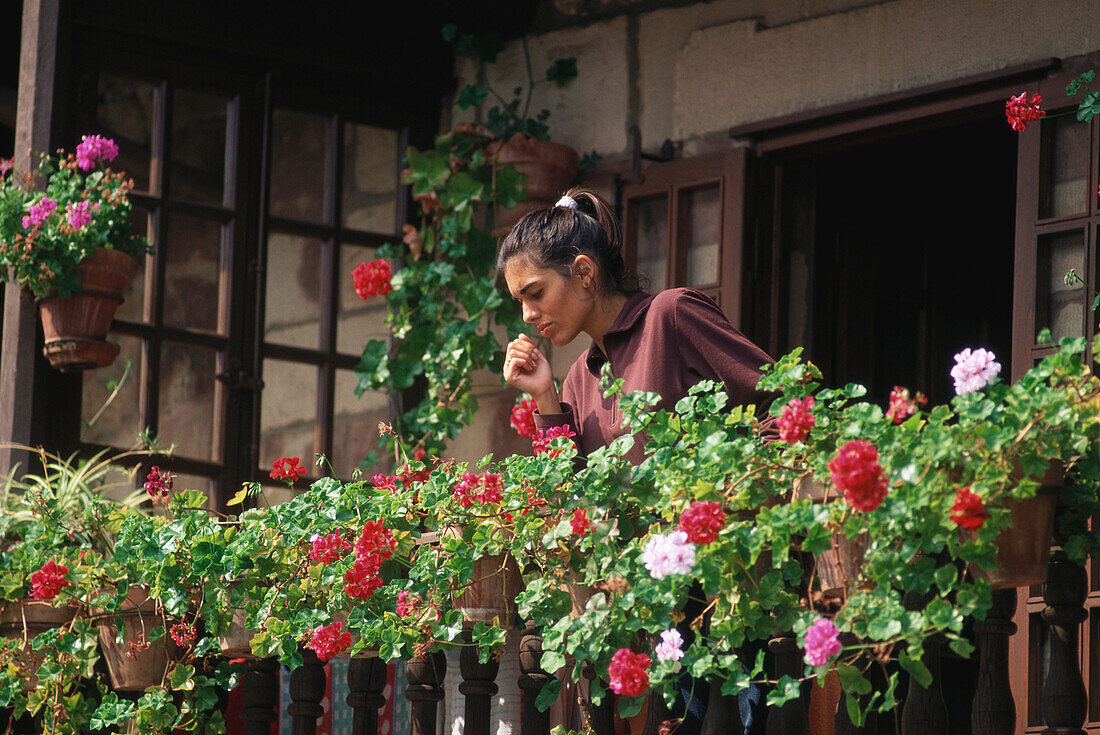 Eine junge Frau gießt Geranien auf dem Balkon eines alten Hauses in Comillas, Kantabrien, Spanien