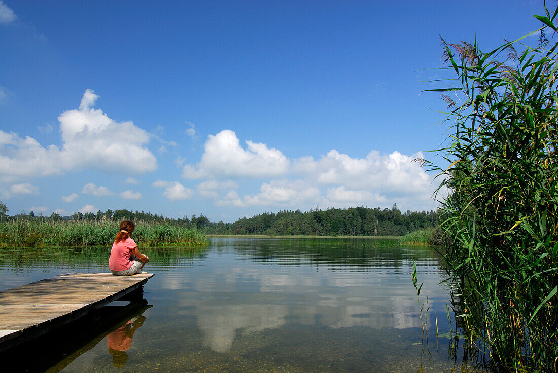 Woman sitting on landing stage at lake Fohnsee, Osterseen, Upper Bavaria, Bavaria, Germany