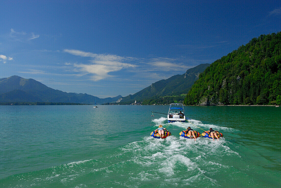 three young women tube riding behind motor boat, lake Abersee, lake Wolfgangsee, Salzkammergut, Salzburg, Austria