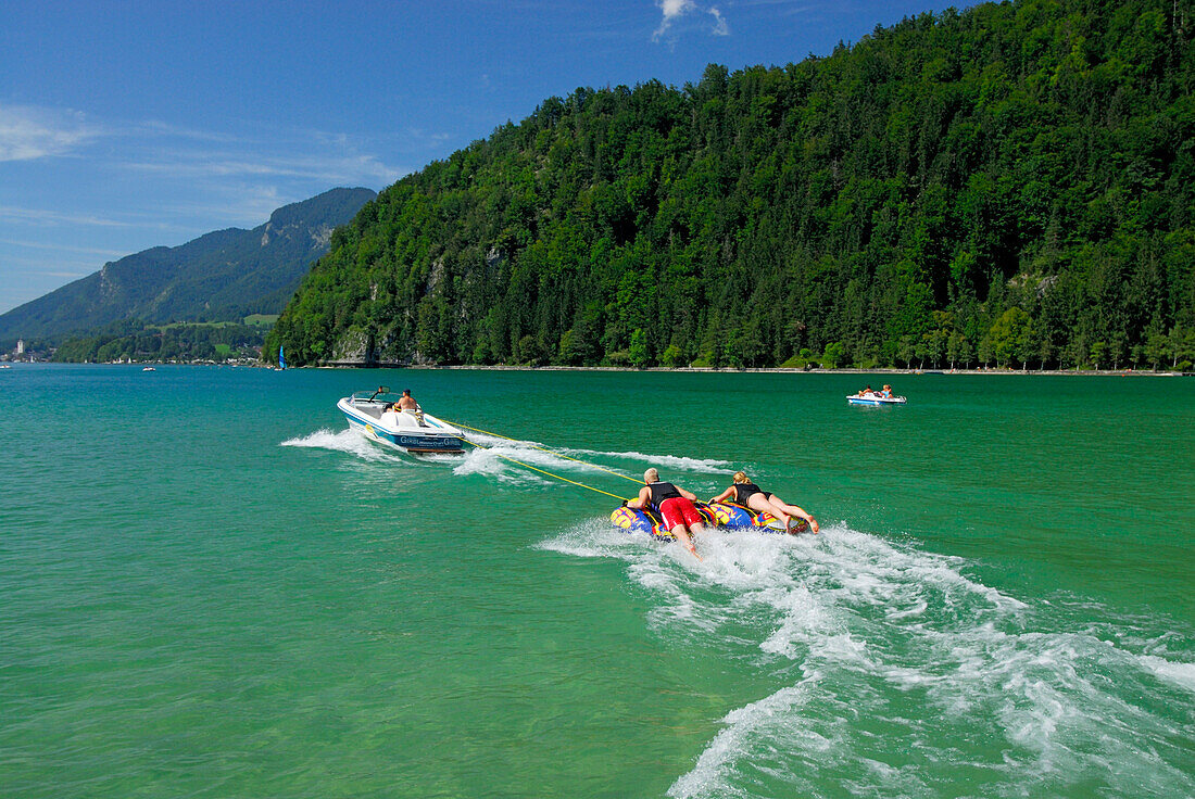 couple tube riding behind motor boat, lake Abersee, lake Wolfgangsee, Salzkammergut, Salzburg, Austria