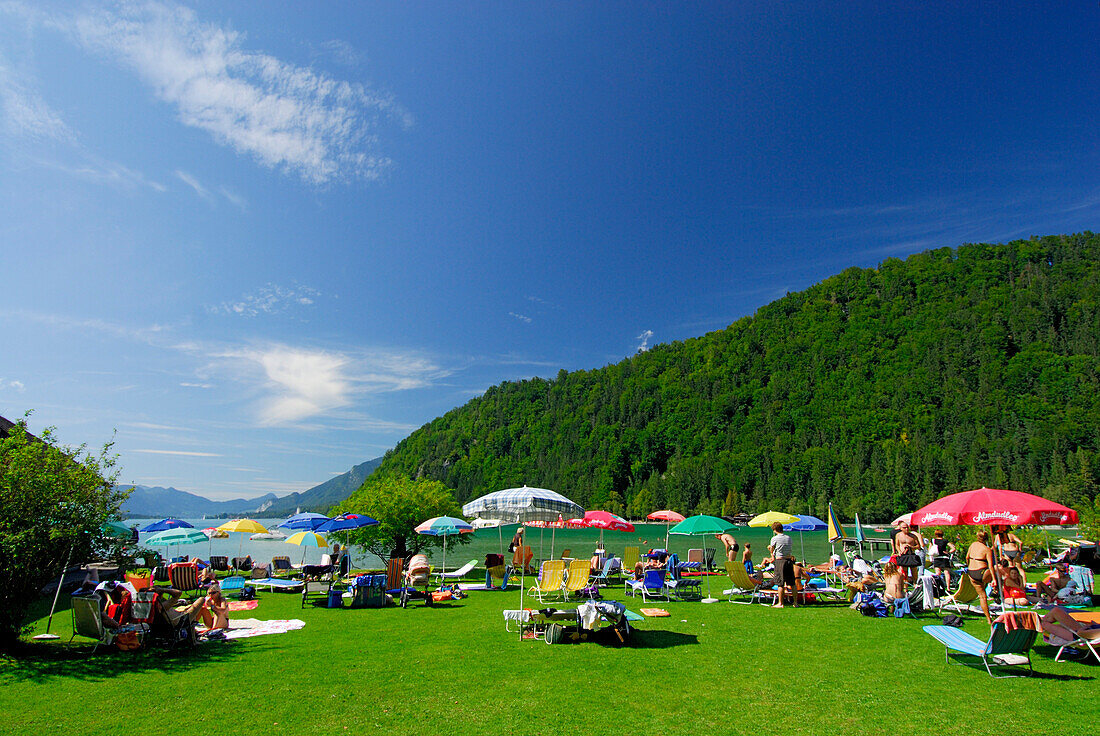 sunbathing area with sunshades and bathers at beach of lake Abersee, lake Wolfgangsee, Salzkammergut, Salzburg, Austria