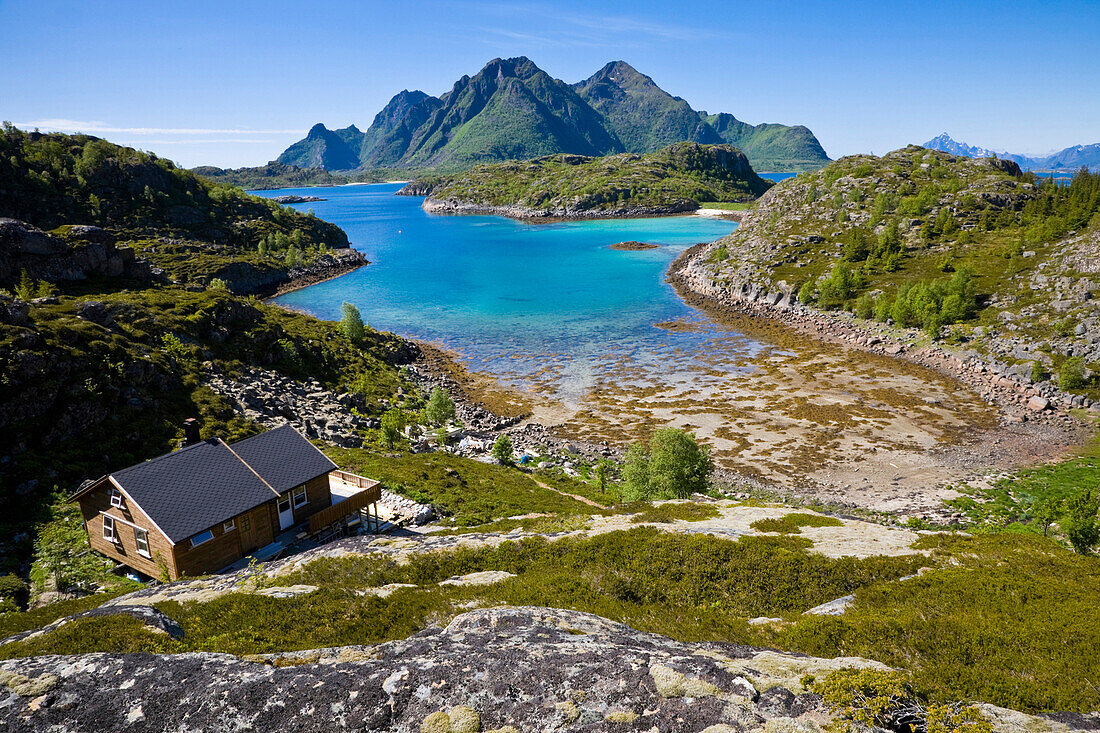 Ein Ferienhaus an einem Fjord der Insel Store Molla, im Hintergrund die Insel Austvagoya, Lofoten, Norwegen