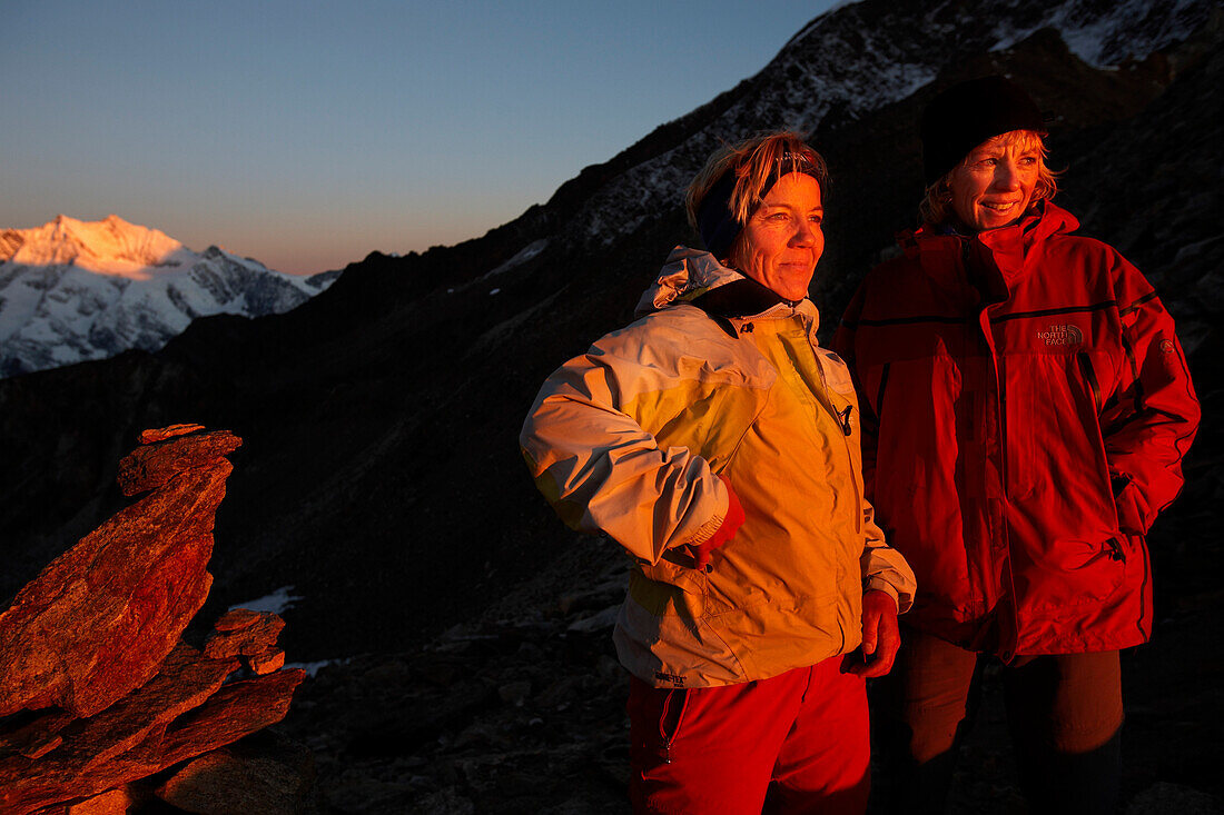 Zwei Frauen, zwei Bergsteigerinnen in der Morgensonne neben einem Steinmann, Zwischenbergpass unterwegs von der Almagellerhütte zum Gipfel des Viertausenders Weissmies, Im Hintergrund die Viertausender der Mischabelgruppe, Wallis, Schweiz MR