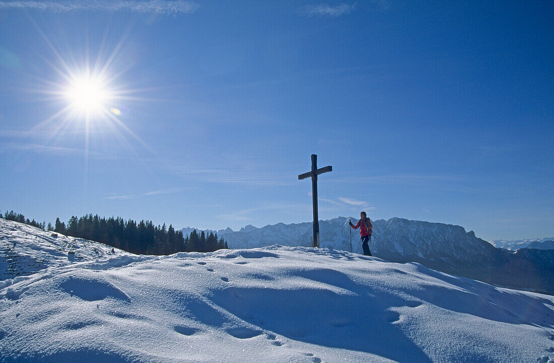 hiker at cross on summit of Karspitze with view to Kaiser range, Chiemgau range, Chiemgau, Upper Bavaria, Bavaria, Germany