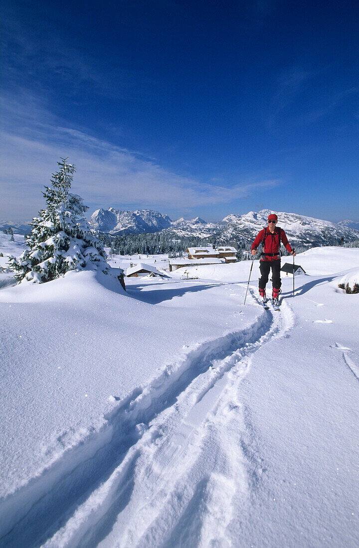 Backcountry skiier in front of deeply snow-covered lodge Straubinger haus with view to Wilder Kaiser range and Unternberghorn, Eggenalm, Fellhorn, Chiemgau range, Chiemgau, Upper Bavaria, Bavaria, Germany